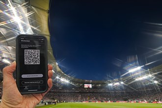 Hand holds smartphone with Luca app for digital contact tracking in packed football stadium