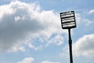 Floodlight mast switched on in front of blue sky with clouds