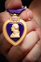 Male hand holding the United States armed forces purple heart medal
