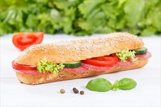 Sandwich baguette wholemeal roll topped with salami ham on wooden board