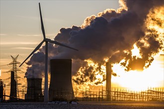 Wind turbine in front of steaming coal-fired power plant at sunset