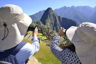 Tourists photograph the ruined city of the Incas and the mountain Huayna Picchu