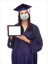 Graduating female wearing medical face mask and cap and gown holding blank computer tablet isolated on a white background
