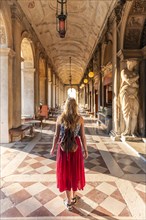 Young woman tourist walking under arcades at St. Mark's Square