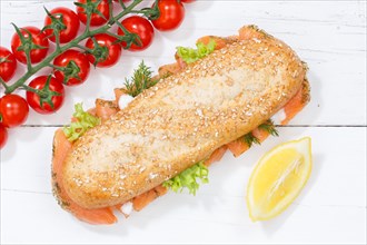 Sandwich baguette wholemeal roll topped with salmon fish from above on wooden board
