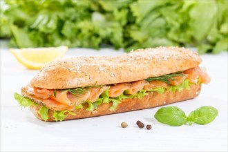 Roll sandwich wholemeal baguette topped with salmon fish on wooden board