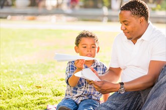 Happy african american father and mixed race son playing with paper airplanes in the park