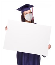 Graduating female wearing medical face mask and cap and gown holding blank poster board isolated on a white background