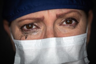 Tearful stressed female doctor or nurse wearing medical face mask on dark background