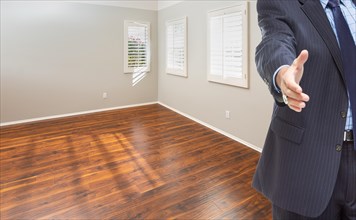 Real estate agent reaches for handshake inside empty room of new house