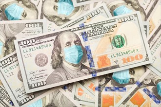 Pile of one hundred dollar bills with medical face mask on face of benjamin franklin