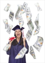 Excited female graduate in cap and gown holding stack of $100 bills with many falling around her on white