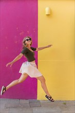 Young woman in dress jumps happily in front of colorful house