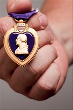 Man holding United States purple heart war medal on a grey background