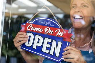 Happy female store owner turning open sign in window