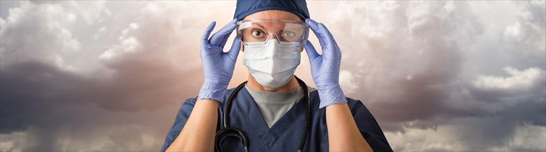Doctor or nurse adjusting safety goggles wearing personal protective equipment over ominous clouds
