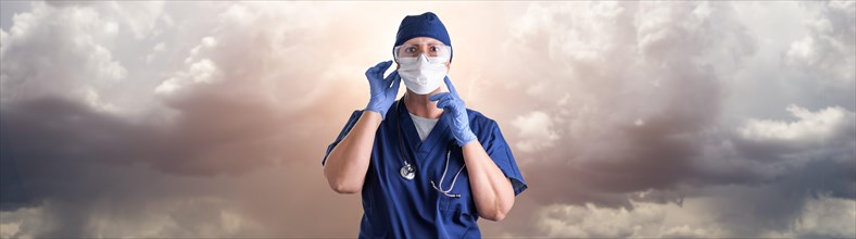 Doctor or nurse adjusting medical face mask wearing personal protective equipment over ominous clouds