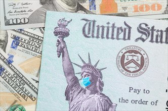 United states IRS stimulus check with statue of liberty wearing medical face mask resting on money