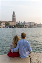 Young couple sitting by the sea enjoying view of St. Mark's Square with Campanile di San Marco