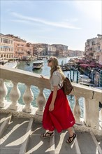 Young woman with red skirt walks over a bridge at the Grand Canal
