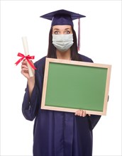 Graduating female wearing medical face mask and cap and gown holding blank chalkboard isolated on a white background
