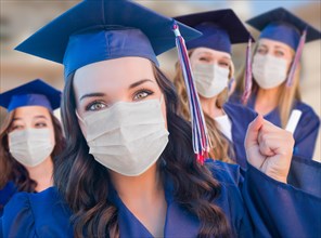 Several female graduates in cap and gown wearing medical face masks