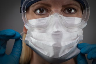 Female Medical Worker Wearing Protective Face Mask and Gear Against Dark Background
