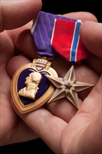 Man holding purple heart and bronze war medals in the palm of his hand