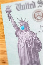 United states IRS stimulus check with statue of liberty wearing medical face mask