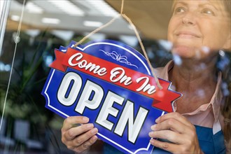 Happy female store owner turning open sign in window