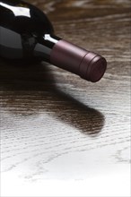 Red wine bottle laying on a wood surface fading down to white