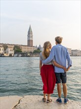 Young couple standing by the sea enjoying view of St. Mark's Square with Campanile di San Marco