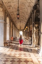 Young woman tourist walking under arcades at St. Mark's Square