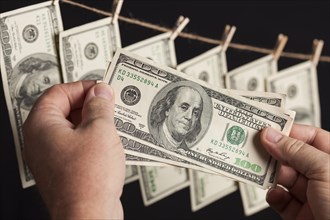 Male hands holding hundred dollar bills with several hanging from a clothesline on a dark background