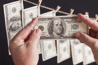 Male hands holding hundred dollar bills with several hanging from a clothesline on a dark background