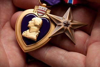 Man holding United States purple heart and bronze war medals in the palm of his hand