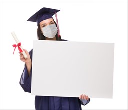 Graduating female wearing medical face mask and cap and gown holding blank poster board isolated on a white background