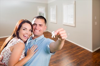 Young military couple showing off house keys in empty room of new home