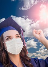 Female graduate in cap and gown wearing medical face mask