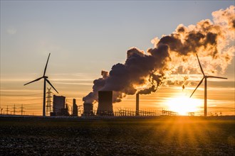 Wind turbines in front of steaming coal-fired power plant at sunset