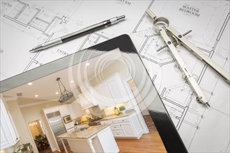 Computer tablet showing finished kitchen sitting on house plans with pencil and compass