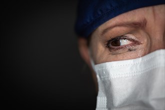 Tearful stressed female doctor or nurse wearing medical face mask on dark background