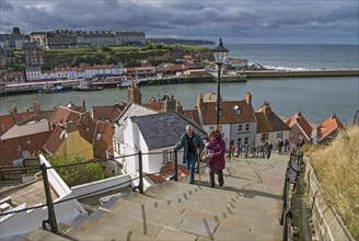 Holiday makers walking up steps in seaside town to Whitby Abbey on clifftop