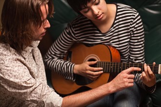 Young male musician teaches female student how to play the guitar