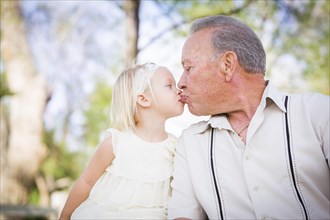 Loving grandfather and granddaughter kissing outside at the park
