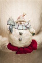 Woman wearing A sweater and seasonal red mittens holding an ornate glass snowman