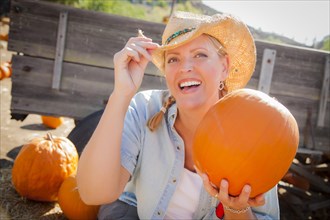 Beautiful blond female rancher wearing cowboy hat holds a pumpkin in a rustic country setting