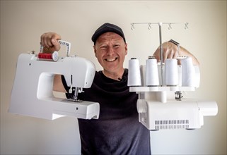 A man holding up a sewing machine and overlock pretending they are very heavy