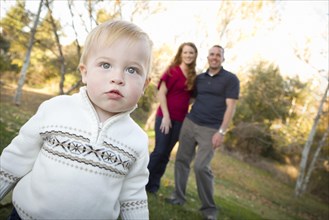 Cute young boy walking in the park as adoring parents look on from behind