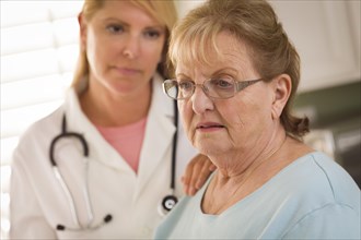 Melancholy senior adult woman being consoled by female doctor or nurse